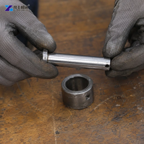 Gloved Hands Holding A Steel Retaining Pin Above A Bushing On A Workbench