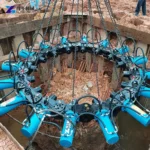 Blue hydraulic pile breaker ring suspended around a concrete pile head